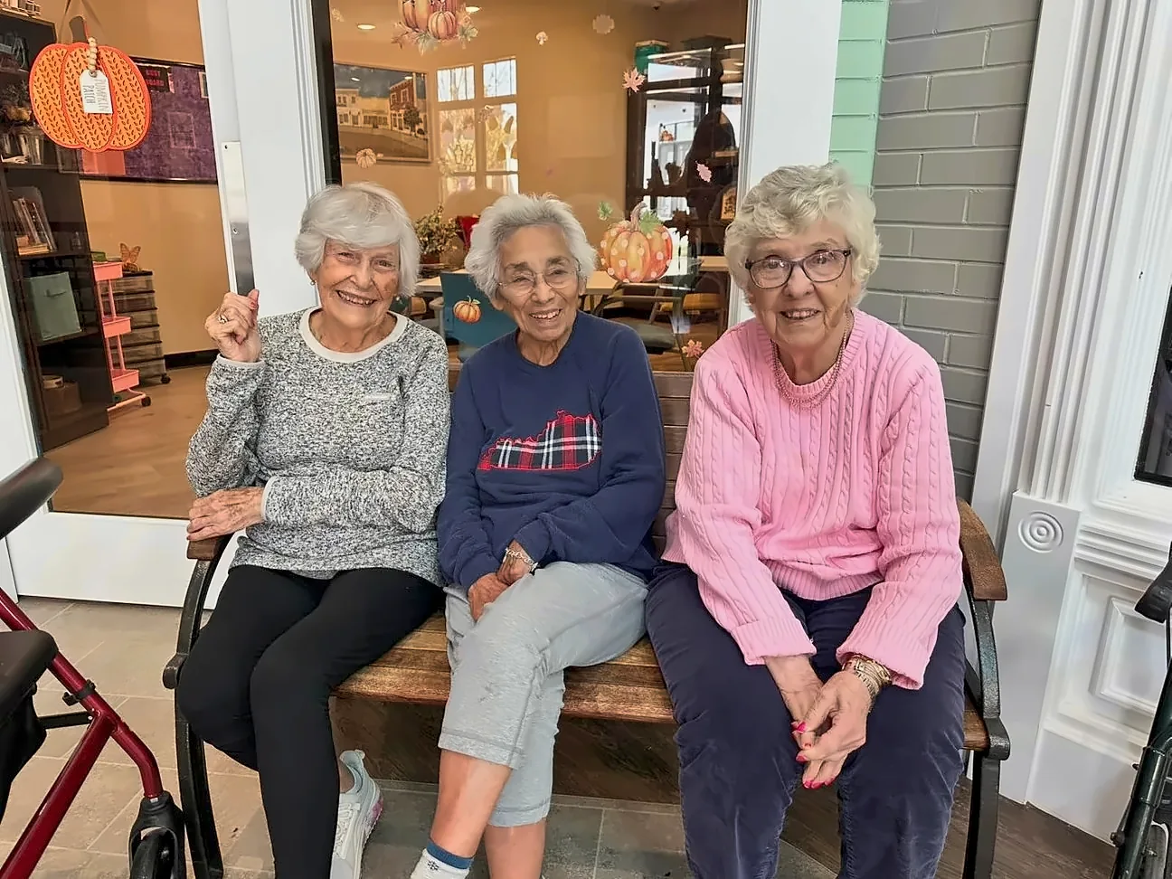 Three memory care residents smiling on a bench in front of a Main Street storefront at Green River Road.