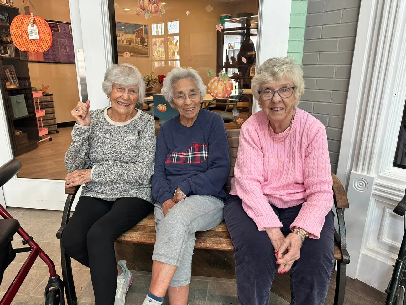 Three memory care residents smiling on a bench in front of a Main Street storefront at Green River Road.